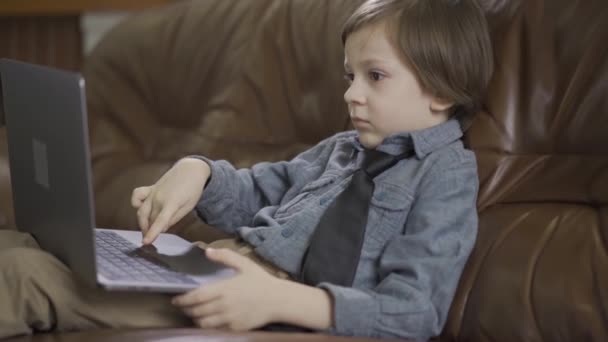 Niño Una Chaqueta Vaquera Sentado Sofá Cuero Jugando Portátil Ocio — Vídeos de Stock