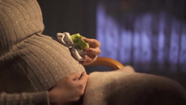 一个身份不明的怀孕女孩坐在黑暗房间里的摇椅上 用一只小婴儿的袜子在肚子上踩踏 — 图库视频影像