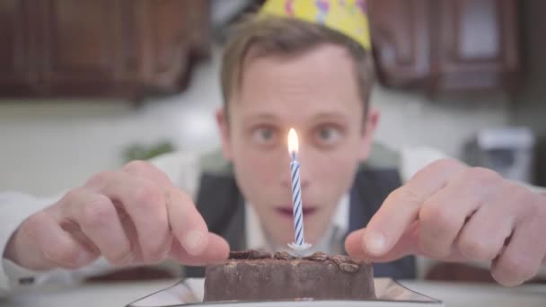 Portret Van Een Grappige Jongeman Met Verjaardagshoed Zittend Voor Een — Stockvideo