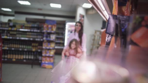 小女儿帮妈妈在超级市场购物 和妈妈一起在超市里的小女孩 女儿帮妈妈在商店里购物 美丽的黑发母亲和一个小女儿在杂货店买食物 — 图库视频影像