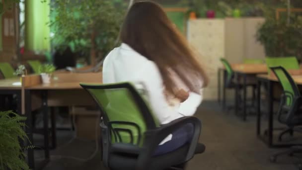 视频中的年轻姑娘 长发在办公椅上纺纱 在办公室里扔文件 动作缓慢 — 图库视频影像