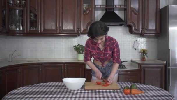 时尚舒适的厨房里 一个穿着别针西服 面带微笑的小女孩在木板上切西红柿 — 图库视频影像