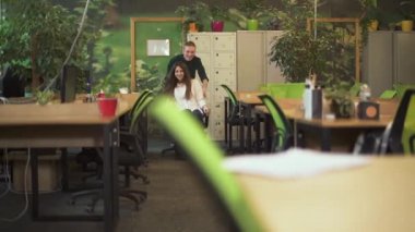 Modern ofiste işten sonra gülümseyen adam ve kadının videosu. Genç adam ofis sandalyesinde oturan güzel kızı götürüyor. 