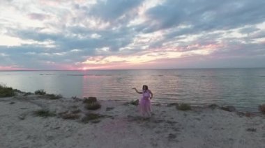 Pembe elbiseli, parlak makyajlı, nehrin kıyısında sis bombalarıyla dans eden tatlı bir genç kadın. Çiçekli, harika bir saç stili olan güzel, şehvetli bir kızın dansı. Yavaş çekim.