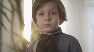 Parlak bir güneşle pencerenin önünde duran boynuna uzun siyah kravat takan sevimli küçük ciddi çocuk. Çocuk, babasını taklit ediyor. Yavaş çekim