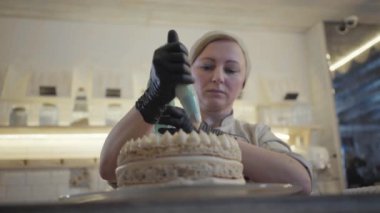 Üniformalı pastacı pastayı süslemek için tatlı krema veya kremalı muhallebi torbası koydu..