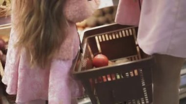 Küçük kızı ve annesi bir sepet tutuyorlar ve yiyecek katlıyorlar. Küçük kız süpermarkette annesine yardım ediyor. Annemle süpermarkette küçük bir kız. Kızı, annesine markette yardım ediyor..