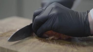 Restoran üniformalı ve siyah eldivenli şefin elleri taze ton balığı dilimleri kesiyor..