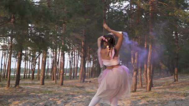 美しいです女の子で明るいメイクでピンクのドレスダンスで煙爆弾で松の木の背景 — ストック動画