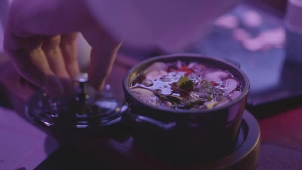 金属製の器にキノコと麺が入ったおいしいスープをカバーするシェフの手は 夜のクラブのテーブルの上に蓋をして青いライトを閉じます パーティーライフスタイル健康食品のコンセプト — ストック動画