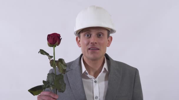 若いです男で建設白い帽子と古典的なスイート与えます長い赤いバラで白い背景 — ストック動画