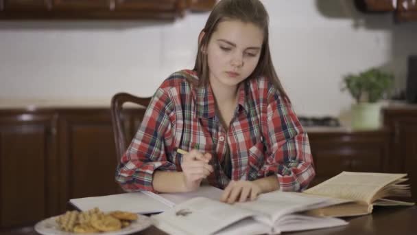 소녀가 책상에 앉아서 숙제를 있습니다 여학생은 책에서 노트에 있습니다 접시에 — 비디오