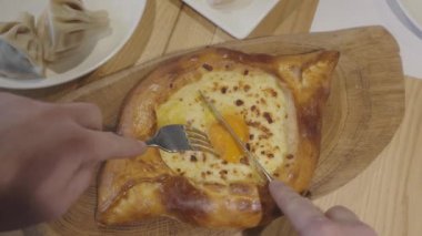 Khachapuri bıçağıyla tahta bir tahtaya uzanmış erkek eli kesiyor..