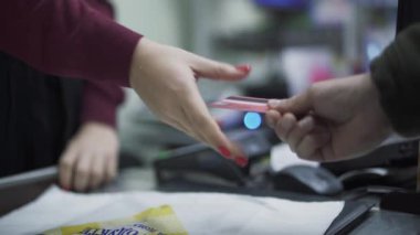 Kredi kartıyla süpermarkette öde. Alıcının eli, kredi kartını satıcısına satar. Satıcının eli terminalden geçen bir kredi kartı taşıyor ve alıcıyı sayıyor..