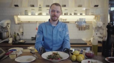 Erkek şef, restoranın profesyonel mutfağının arka planında yeni hazırlanmış karabuğday eriştesi ve sebze tabağını sunar.