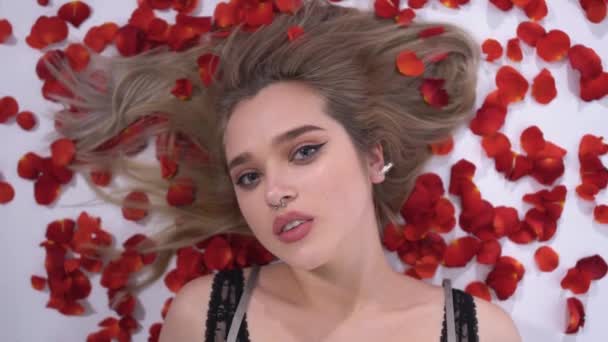 Portrét mladé dívky s piercing v nose na pozadí okvětních lístků červené růže zblízka, video 