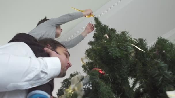 Kleine Jongen Hangt Kerstspeelgoed Aan Boom Zittend Zijn Vaders Nek — Stockvideo