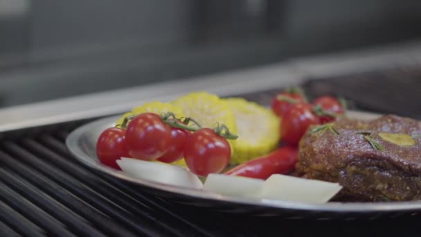 A tányér a hús, kukorica, cseresznye paradicsom, citromfű és chili paprika feküdt a grill közeli. Ételkészítés egy modern étteremben. A kamera jobbra mozog.