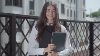 Terasta elinde dizüstü bilgisayarla kameraya bakan güzel bir kadının portresi. 