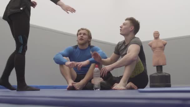 Δύο Αθλητικοί Άντρες Κάθονται Στο Πάτωμα Του Γυμναστηρίου Και Ξεκουράζονται — Αρχείο Βίντεο