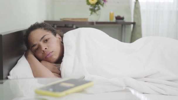 Vídeo Somnolienta Mujer Afroamericana Bajo Una Manta Blanca Sala Luz — Vídeo de stock