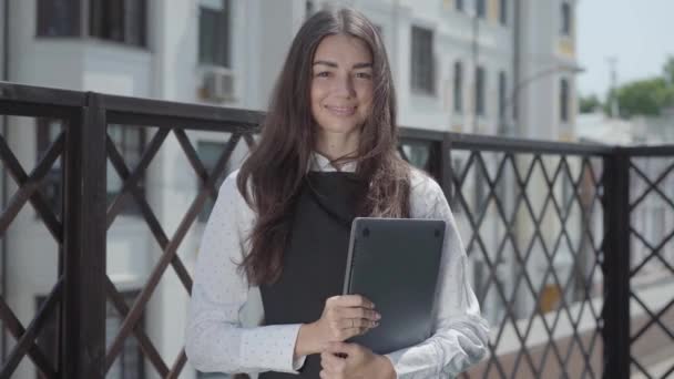 一个漂亮的年轻女子站在阳台上 手拿着笔记本电脑 视频看着摄像机的画像 — 图库视频影像