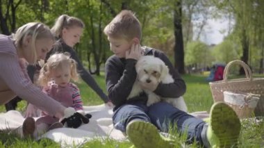 Çocuklarla birlikte iki genç anne bahar günü doğada yeşil muhteşem bir parkta battaniyenin üzerinde oturuyorlar. Anne ve oğul, anne ve kız piknikte. Beyaz tüylü köpek yakınlarda uzanıyor. Aileler arasındaki arkadaşlık kavramı.