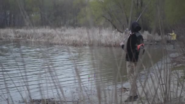 街の近くの川で釣りを回転早朝にカーキパンツで若い漁師を自信を持って — ストック動画