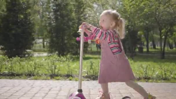 Mała Zabawna Dziewczyna Różowej Sukience Jeżdżąca Skuterze Parku Kamera Śledzi — Wideo stockowe