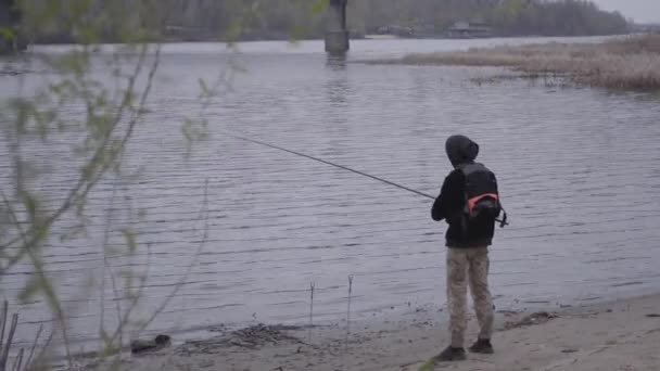 街の近くの川で釣りを回転早朝にカーキパンツの若い焦点を当てた釣り人を自信を持って — ストック動画