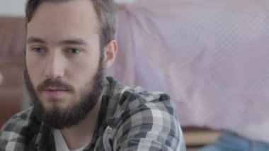 Mutlu eş eşarp ve video eşliğinde ön planda oturan sakallı bir adamın portresi.