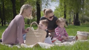 Çocuklarla birlikte iki genç anne bahar günü doğada yeşil muhteşem bir parkta battaniyenin üzerinde oturuyorlar. Anne ve oğul, anne ve kız piknikte. Beyaz tüylü köpek yakınlarda uzanıyor. Aileler arasındaki arkadaşlık kavramı.