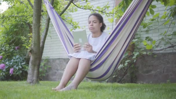 Mujer Afroamericana Joven Sentada Hamaca Relajándose Jardín Mensajes Texto Tableta — Vídeos de Stock