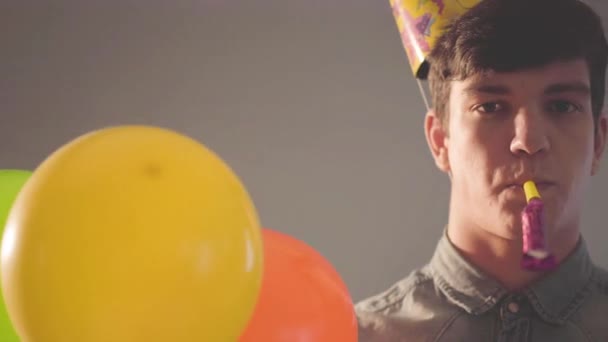一个戴着生日礼帽的年轻人拿着气球看着摄像机的特写 派对上的那个人 庆祝一下 相机向右移动 — 图库视频影像