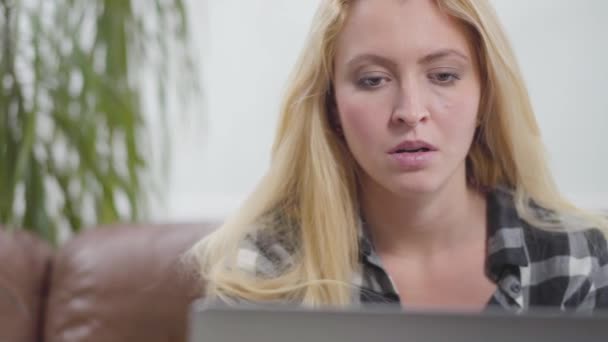 Het Blonde Meisje Zit Thuis Een Leren Bank Voor Laptop — Stockvideo