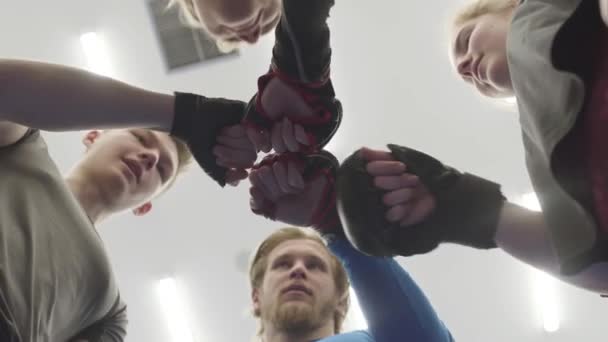 ジムのカメラの上の円の中に立っている4人 男性と女性の選手の会社が一緒に手袋に彼らの拳を置きます チームスピリットのコンセプト 以下の図 — ストック動画