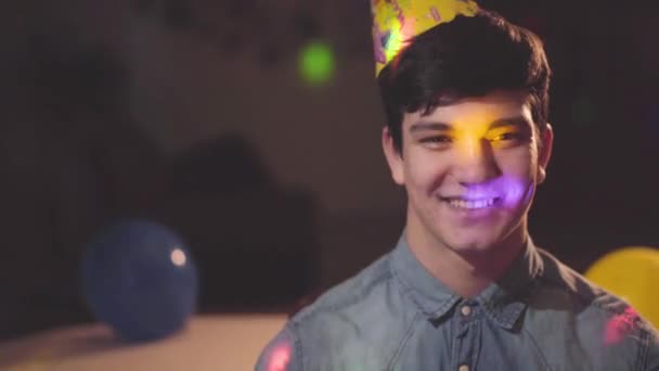 Retrato Joven Sonriente Con Sombrero Cumpleaños Mirando Cámara Luces Brillantes — Vídeos de Stock