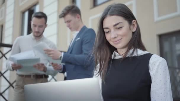 一个漂亮的年轻女子的肖像在前景与笔记本电脑一起工作 两名男子在后台讨论文件 业务关系 自由职业 远程工作 视频概念 — 图库视频影像