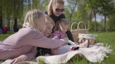 Çocuklarla birlikte iki genç anne bahar günü doğada yeşil muhteşem bir parkta battaniyenin üzerinde oturuyorlar. Anne ve oğul, anne ve kız piknikte. Beyaz tüylü köpek yakınlarda uzanıyor. Aileler arasındaki arkadaşlık kavramı.