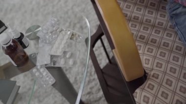 Tanınmayan çocuk koltukta sallanıyor, elinde yumuşak bir oyuncak, haplarla dolu bir masa, video