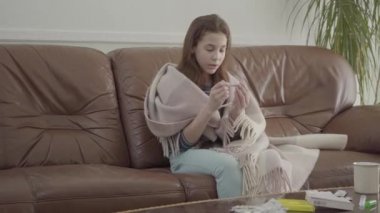 Küçük hasta kız deri koltuğa, tabletlere, haplara ve masaya oturur. Termometreye bakan kadın, video 