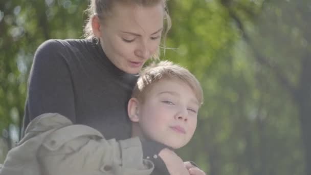 幼い母親と10代の息子が公園で一緒に休んでいる 頬に子供のキスをしている女性 少年は彼女の背中にキスをします 幸せな家族だ屋外レジャー — ストック動画