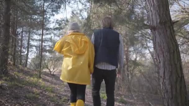 男人和女人手牵着手在春天的森林里散步的背影 戴帽子 穿黄靴和外套的女人 — 图库视频影像