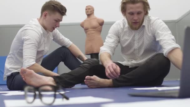 Dos Hombres Sentados Suelo Gimnasio Papeles Anteojos Delante Maniquí Está — Vídeo de stock