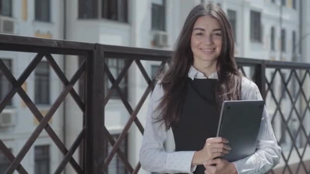 一个漂亮的年轻女子站在阳台上 手拿着笔记本电脑 视频看着摄像机的画像 — 图库视频影像
