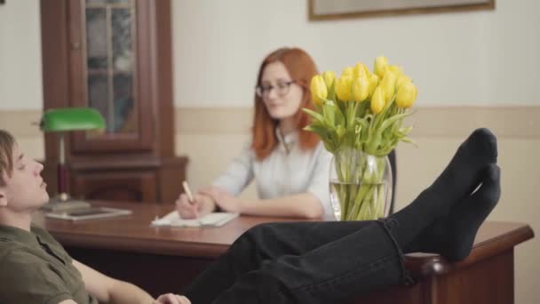 松了口气的年轻人坐在心理医生的办公室里 双脚放在桌子上 告诉她他的问题 女心理学家咨询她的青少年病人 — 图库视频影像