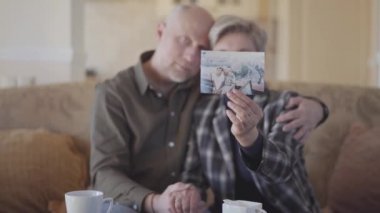 Kanepede oturan yetişkin bir çift eski fotoğraflarını inceliyor ve anılarını paylaşıyor..