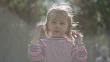 Ön planda, taçlı, baş aşağı duran, ileriye bakan tatlı küçük kız. Dışarıda oynayan sevimli komik prenses. Arka planda bulanık anne var.