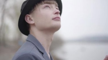 Ceketli genç bir balıkçı portresi ve kentin yakınlarındaki bir nehirde sabahın erken saatlerinde ağzına kadar dolu bir şapka. Olta ve makara. Nehirde uçan balıkçı