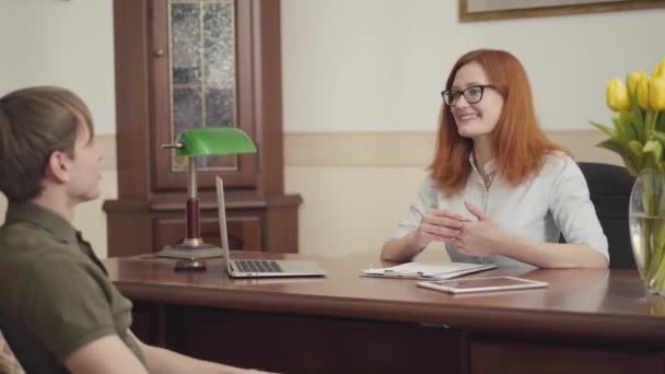 年轻人坐在心理医生的办公室里 回头看 戴眼镜看病人时迷人的红头发女心理学家 — 图库视频影像